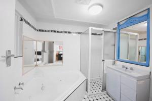 a white bathroom with a tub and a sink and a shower at Manly Waves Studios & Apartments in Sydney
