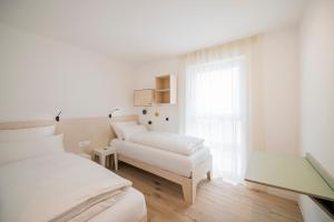 a white bedroom with two beds and a window at stella alpina in Dobbiaco