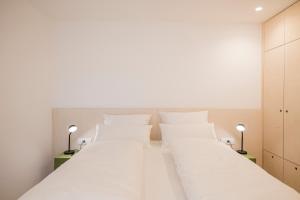 two beds in a bedroom with white walls and lamps at stella alpina in Dobbiaco