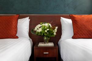 a vase of flowers on a table between two beds at Rydges Auckland in Auckland