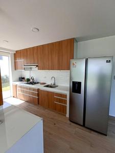 a kitchen with a stainless steel refrigerator and wooden cabinets at HOP ODAIBA exclusiva laguna y playa en Chincha in Chincha Baja