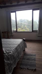 ein Schlafzimmer mit einem Bett und einem großen Fenster in der Unterkunft Chalé Sabiá in Aiuruoca