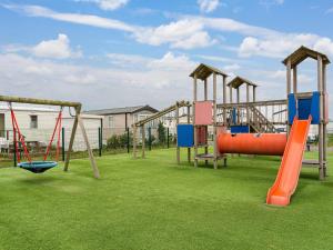 ein leerer Spielplatz mit einer orangefarbenen Rutsche und Schaukeln in der Unterkunft Modern mobile home in Middelkerke with garden in Middelkerke