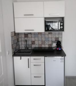 eine weiße Küche mit einer Spüle und einer Mikrowelle in der Unterkunft Werner Apartman in Mohács
