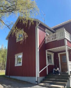 a woman sitting on the front porch of a red house at Surrounded by nature in Bjurholm in Bjurholm