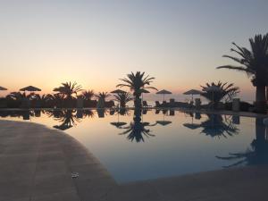 une piscine avec des palmiers et un coucher de soleil en arrière-plan dans l'établissement Georgia Vicky Studios & Apartments, à Stavros