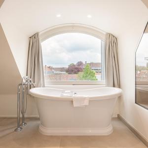 a white bath tub sitting next to a window at De Tuilerieën - Small Luxury Hotels of the World in Bruges