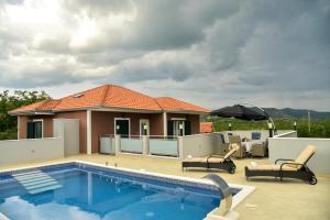 a house with a swimming pool and two chairs and an umbrella at VILLA REBECCA, Muć - Split in Gornji Muć