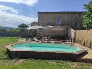 a swimming pool in front of a stone building with umbrellas at Entre blé et lavande in Bonnieux