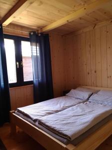 a bed in a wooden room with two windows at Przystań Kajakowa Zakole in Buda Ruska