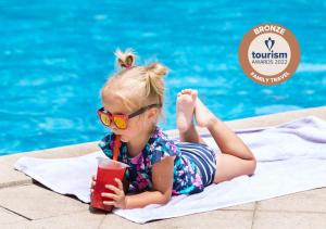 a little girl laying on a towel next to a swimming pool at Acrotel Athena Pallas in Elia