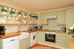 una cocina con armarios verdes y electrodomésticos blancos en Balnagown Estates Gardener's Cottage, en Kildary