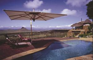 a pool with an umbrella and a chair and a table and a chair at Isandlwana Lodge in Hlazakazi