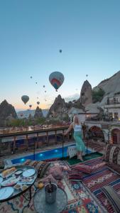 uma mulher de pé numa varanda com balões de ar quente em Local Cave House Hotel em Goreme