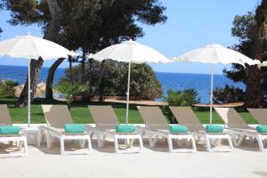 Iberostar Selection Santa Eulalia Adults-Only Ibiza في سانتا إيولاليا ديل ريو: صف من كراسي الصالة والمظلات مع المحيط