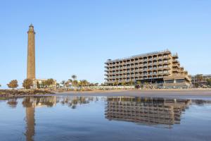 a building and a tower on a beach with a body of water at Hotel Faro, a Lopesan Collection Hotel - Adults Only in Maspalomas