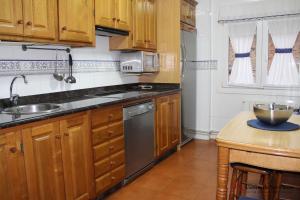 cocina con armarios de madera, fregadero y lavavajillas en VUT La Fuentina -Casas de los Picos, en Panes