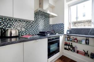 uma cozinha com armários brancos e um forno com placa de fogão em Bright and stylish apartment in trendy Islington by UnderTheDoormat em Londres