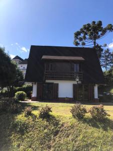 a house with a black roof on a grass field at Chalé Sonho da Vovó a 5 minutinhos do Centrinho de Capivari in Campos do Jordão