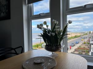 een vaas met bloemen op een tafel voor een raam bij Seafront Luxury Apartment in Cleethorpes