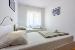 a white bedroom with two beds and a window at Apartment Arya in Crikvenica
