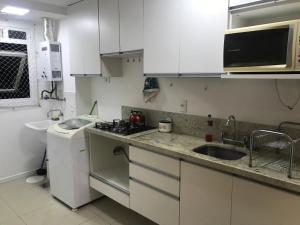 una pequeña cocina con armarios blancos y fregadero en Apartamento p/ 8 com garagem churasqueira e piscina en Porto Alegre