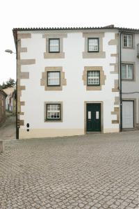 a white building with a black door on a cobblestone street at Casa da Praça - Guest House in Pinhel