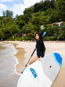 a woman standing on a beach holding a surfboard at Novotel Phuket Kamala Beach - SHA Extra Plus in Kamala Beach