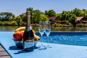 una bottiglia di vino e due bicchieri su un tavolo a bordo piscina di Kővágó Vendégház Nagyfoki holtág a Szarvas