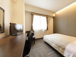 ein Hotelzimmer mit einem Bett und einem Schreibtisch mit einem TV in der Unterkunft Atsugi Urban Hotel in Atsugi