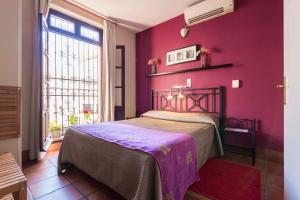1 dormitorio con pared morada, cama y ventana en Hotel Patio de las Cruces, en Sevilla