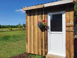 a wooden shed with a door and flowers in a field at Double Decker Bus on an Alpaca farm sleeps 8 in Bovey Tracey