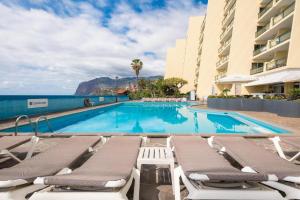 einen Pool mit Chaiselongues neben einem Gebäude in der Unterkunft Tranquil Beachside Stay - Atlantic Gardens Beach in Funchal