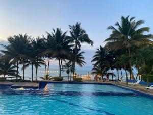 a large swimming pool with palm trees and the ocean at Suites de Lujo Playa Azul in Tonsupa