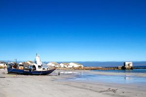 un barco sentado en la arena de la playa en DE SWARTE MOSSEL, en Hondeklipbaai