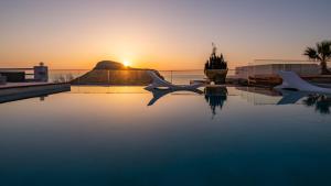 a swimming pool with the sunset in the background at Arkasa Palace in Arkasa
