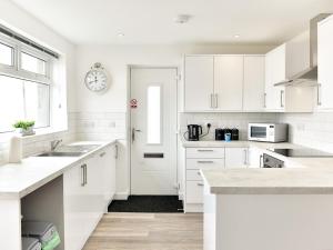 a white kitchen with white cabinets and a clock on the wall at Pass the Keys Newly Renovated Bungalow - Stunning views of Gower in Swansea