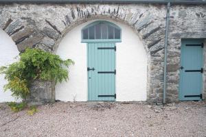 a building with a green door next to a stone wall at Steading Cottage - 50m from the beach in Port Appin