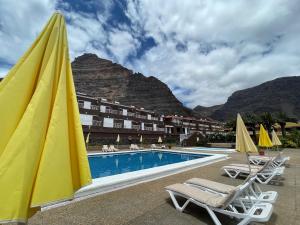 un complejo con piscina, sillas y montaña en Apartamentos Los Tarajales, en Valle Gran Rey