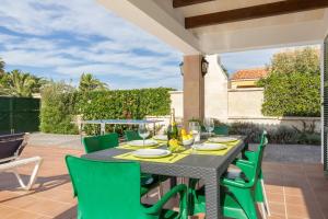 a patio with a black table and green chairs at Villa S'Aladern in Cala'n Bosch