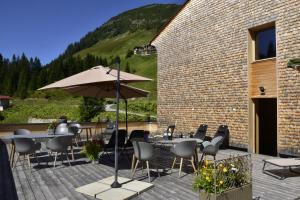 un patio con tavoli, sedie e un ombrellone di Am Gehren - Arlberg Appartements a Warth am Arlberg
