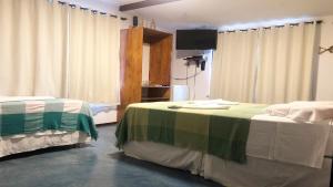 een kamer met 2 bedden, gordijnen en een televisie bij Pousada do Sol in Lagoinha