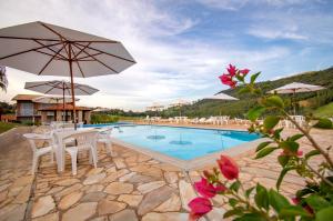 a swimming pool with white chairs and an umbrella at Filimahalo Hotel in Serra Negra