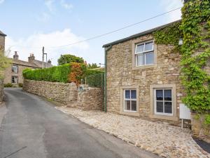 a stone house with a stone wall next to a street at Carn Cottage in Long Preston