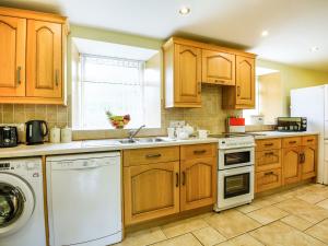 a kitchen with wooden cabinets and a white dishwasher at Y Bwthyn in Llanegryn