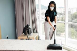 a woman in a mask is vacuuming a bed at Cozy Home with Spectacular View in Bayan Lepas