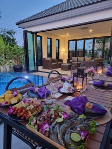 - une table avec des assiettes de nourriture à côté d'une piscine dans l'établissement BAAN DALAH POOL VILLA, à Buriram