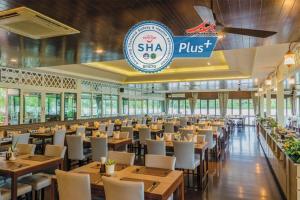 a restaurant with wooden tables and white chairs at Baan Amphawa Resort & Spa - SHA Certified in Amphawa
