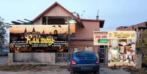 un'auto parcheggiata di fronte a un edificio con un cartellone pubblicitario di Mini-hotel Kamianets a Kam"janec'-Podil's'kyj