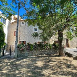 a building with a tree and a stone wall at La Belle Histoire in Bize-Minervois